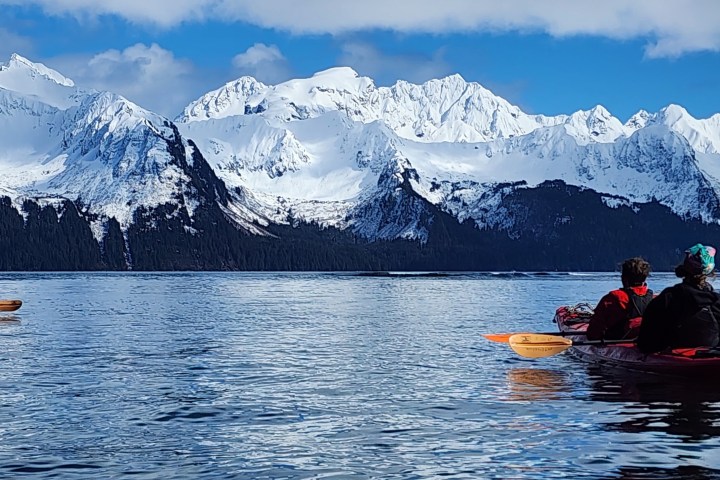 Kayakers on a lake with snow-capped mountains in the background.