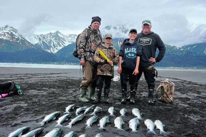 Four people stand on a beach with mountains, posing behind rows of fish lying on the sand.