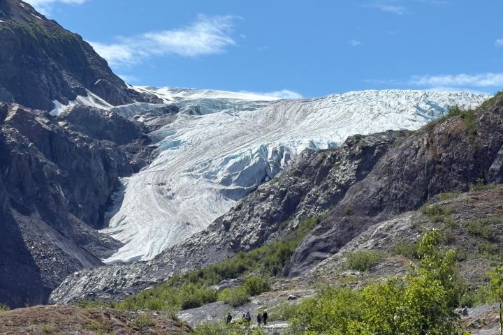 Glacier with rocky mountains under blue sky, hikers below