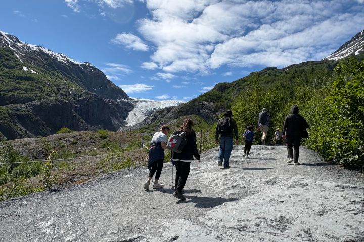 Group of people walking on a mountain trail towards a glacier.
