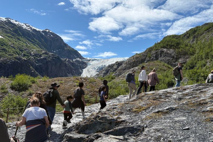 Group hiking towards a glacier under a blue sky with clouds.
