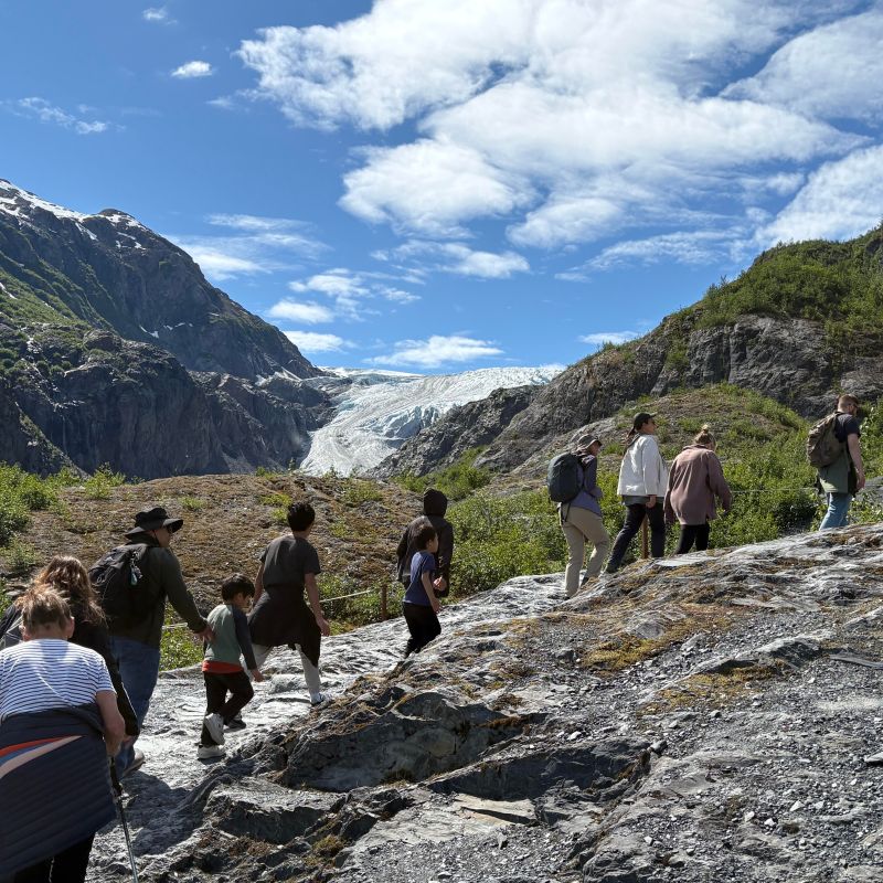 Group hiking towards a glacier under a blue sky with clouds.
