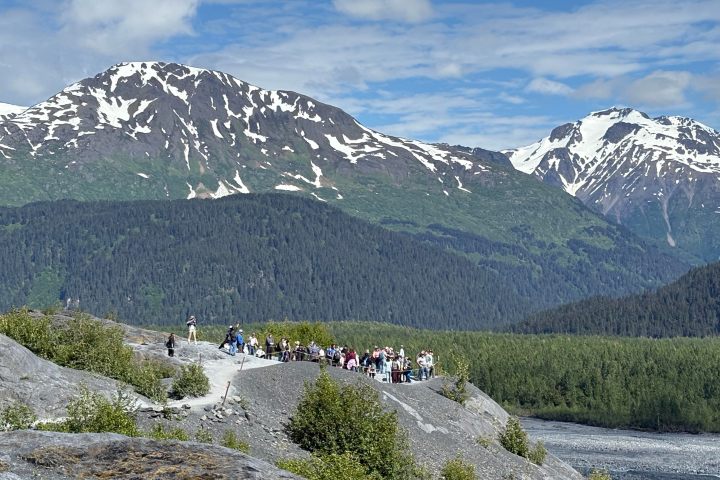 Group of people hiking on mountain trail with snow-capped peaks in the background.
