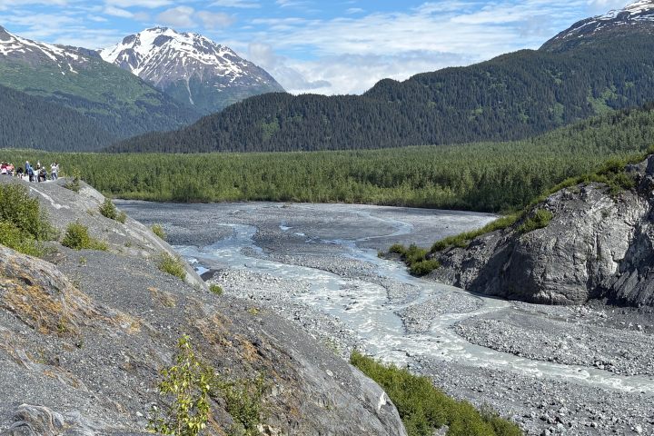 Mountain landscape with a winding river and forest under a partly cloudy sky.