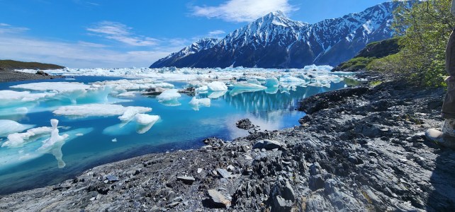 Snowy mountains and turquoise lake with icebergs under a blue sky.