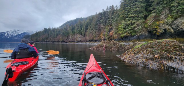 Two kayaks on a calm lake surrounded by forested hills and cloudy sky.