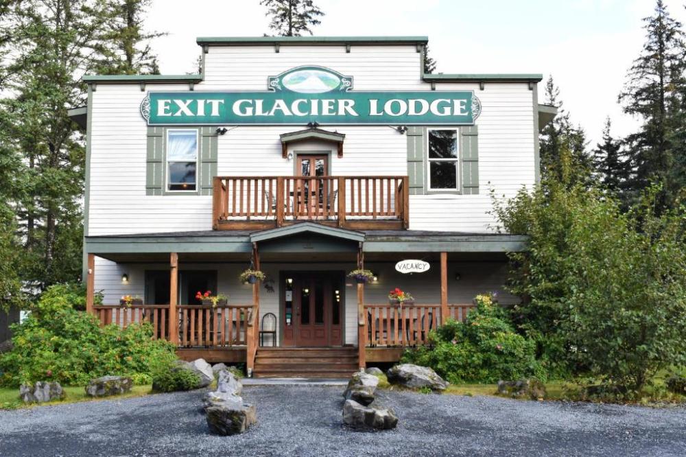 Two-story lodge with 'Exit Glacier Lodge' sign, wooden porch, surrounded by trees.