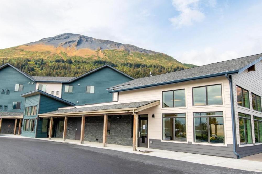 Modern building with large windows under a mountain and blue sky.