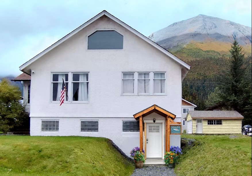 White house with wooden entrance, American flag, mountain backdrop.