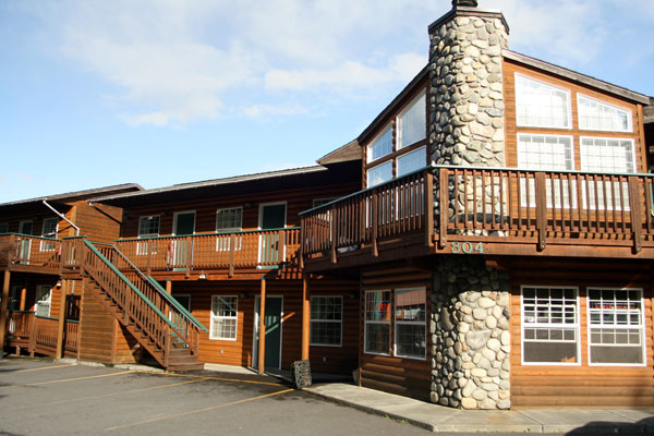 Two-story wooden building with stone chimney and balcony.