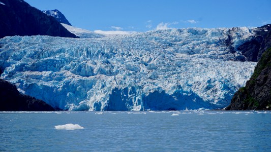 Large glacier with icy blue tones surrounded by mountains and calm water.